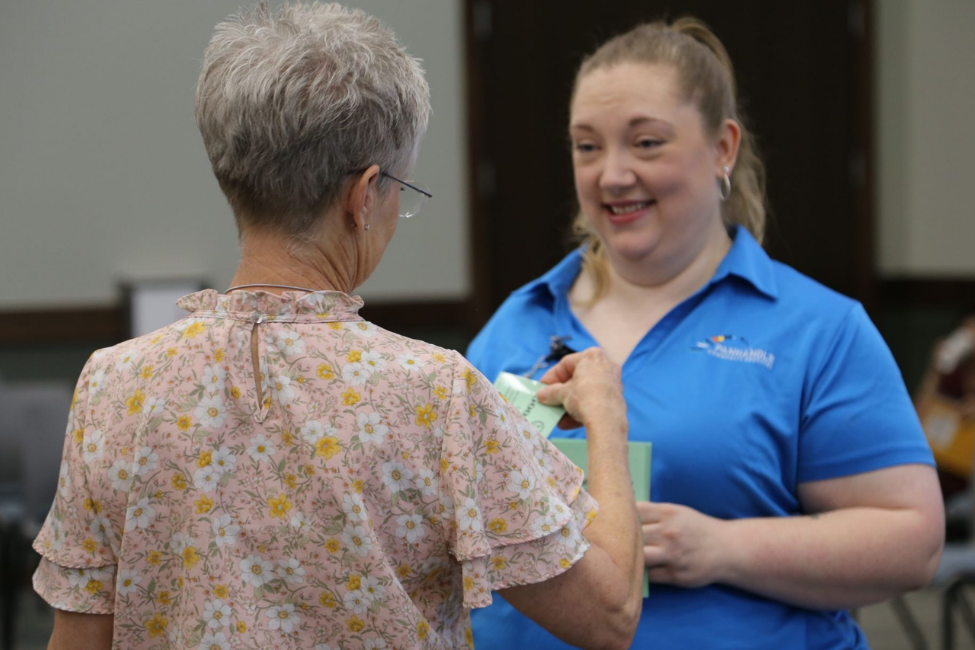 Woman handing a card to another person at a community event