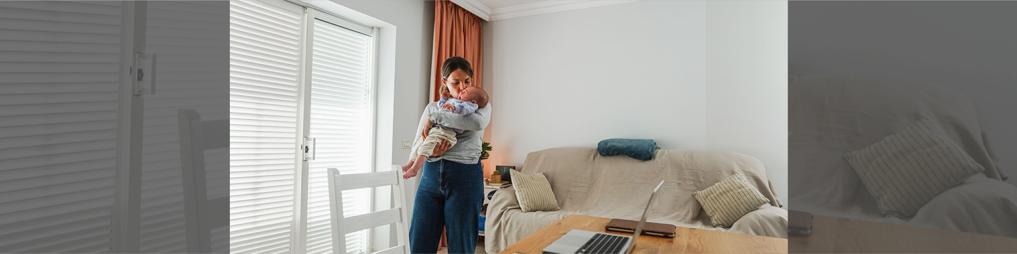 Mother holding a baby in a living room with a laptop nearby