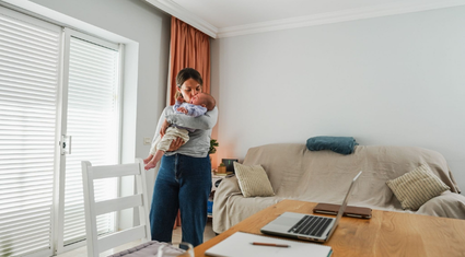 Mother holding a baby in a living room with a laptop nearby